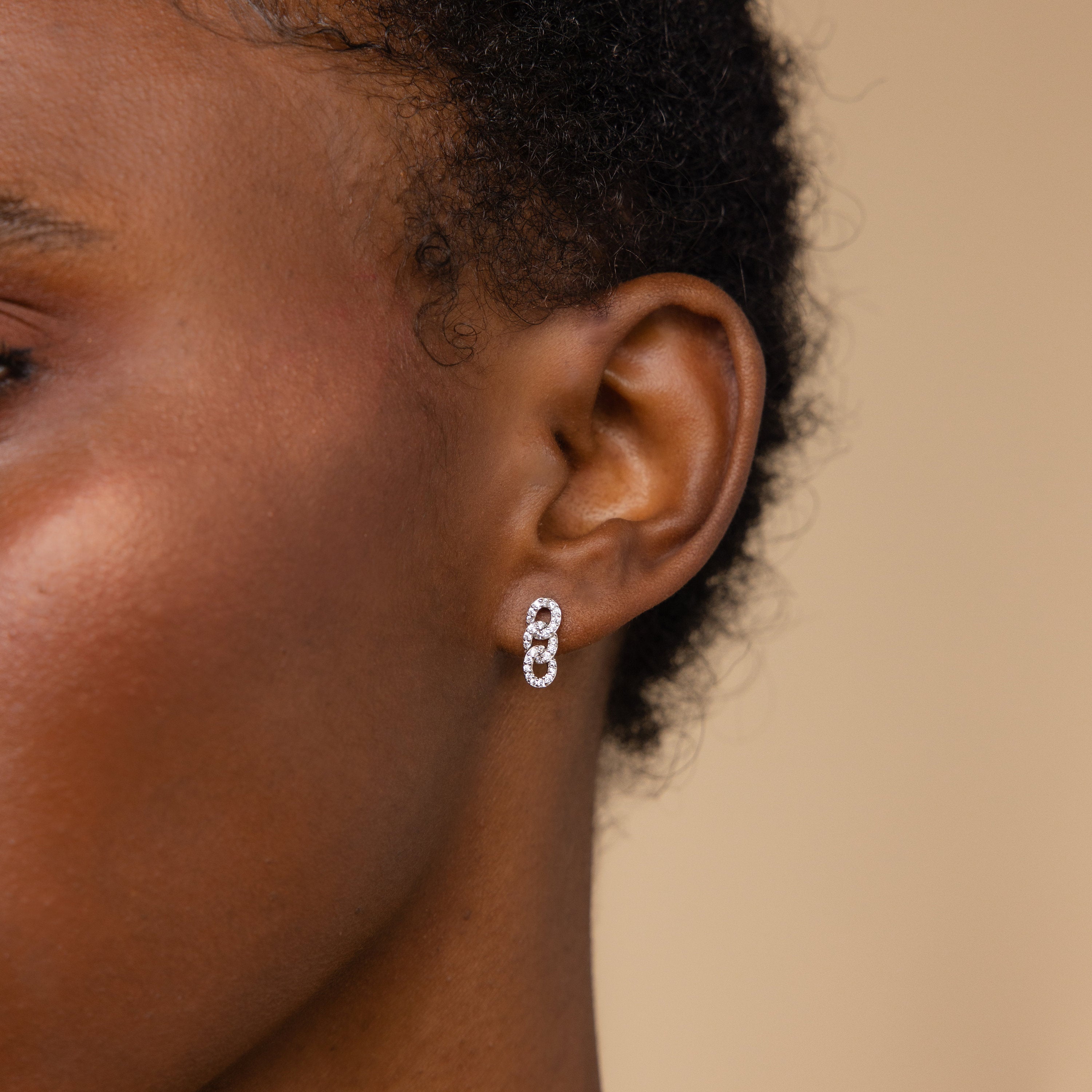 Close-up of a person's ear wearing elegant Pave Link Studs, featuring small double hoops with diamond pavé, set against a neutral background.
