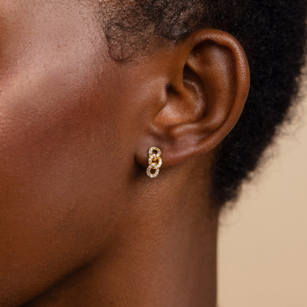 Close-up of a person wearing Pave Link Studs—gold and diamond earrings with interlocking links, perfect for pairing with your favorite necklace.
