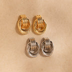 Two pairs of Triple Knot Earrings, in gold and silver, displayed on a beige textured background—an ideal anniversary gift.