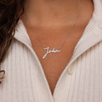 A woman wears a white sweater and the Pave Handwriting Necklace featuring the name Julia in elegant cursive—a striking statement piece.