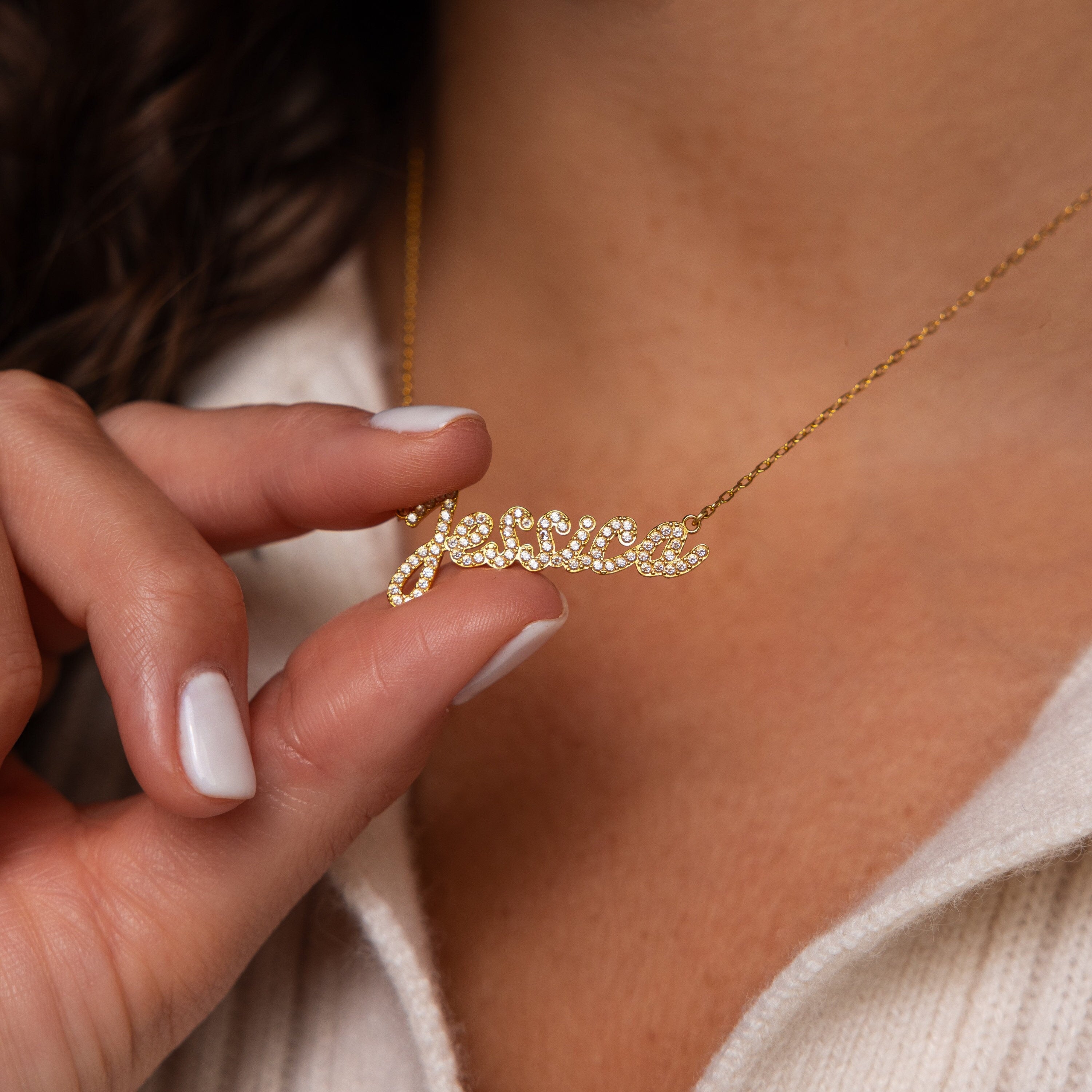 A person holds a sparkling Pave Handwriting Necklace in the name Jessica, featuring dazzling stones—the ideal choice for statement jewelry.