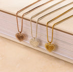 Three Pave Fingerprint Heart Necklaces in rose gold, silver, and gold sit on a beige-covered book—each personalized with a fingerprint for a unique touch.