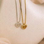 The Pave Fingerprint Heart Necklace features two heart-shaped pendants, one silver and one gold, on matching chains—perfect for a personalized look against a neutral background.