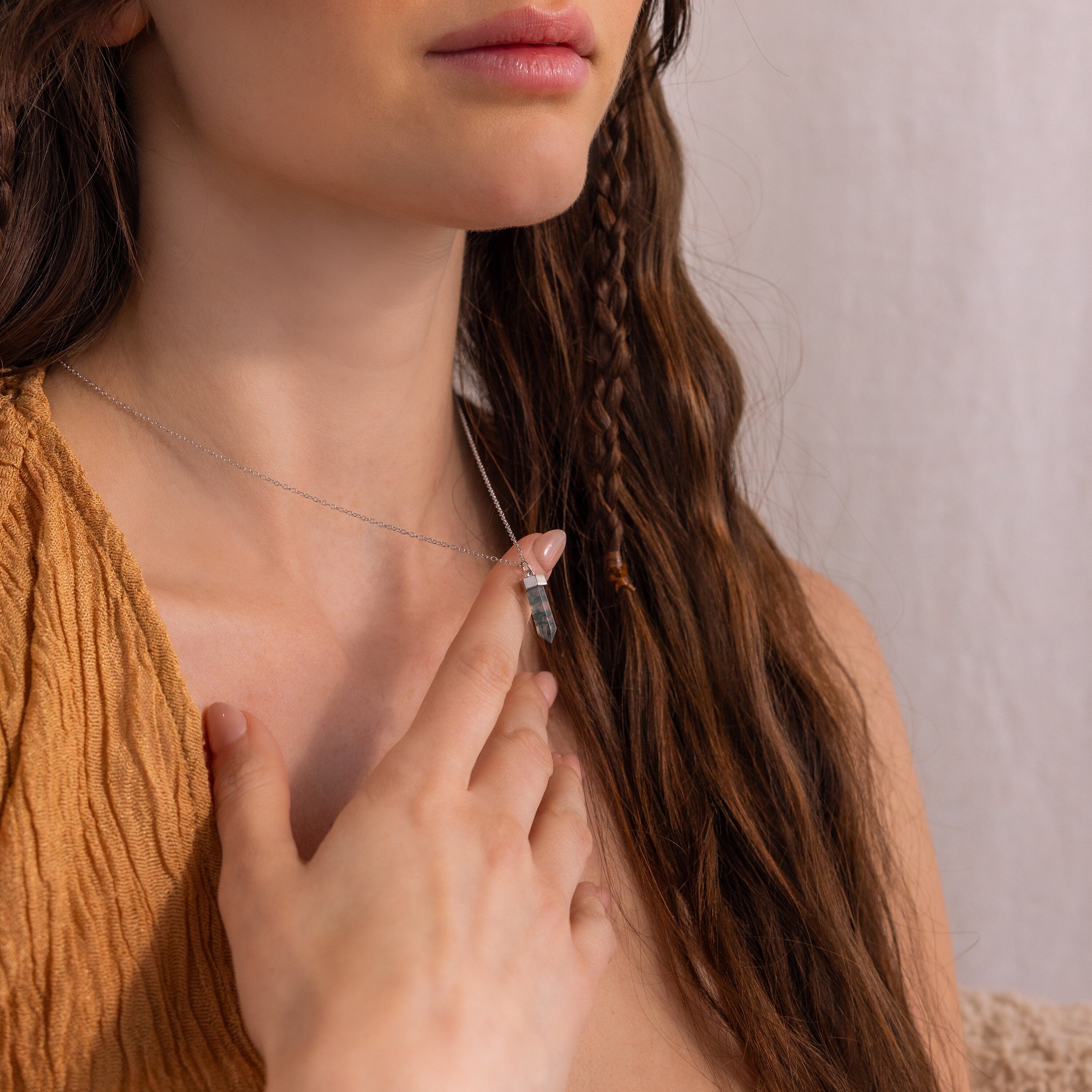 A woman with long brown hair touches her marbled Agate Quartz Necklace while wearing a textured tan top.