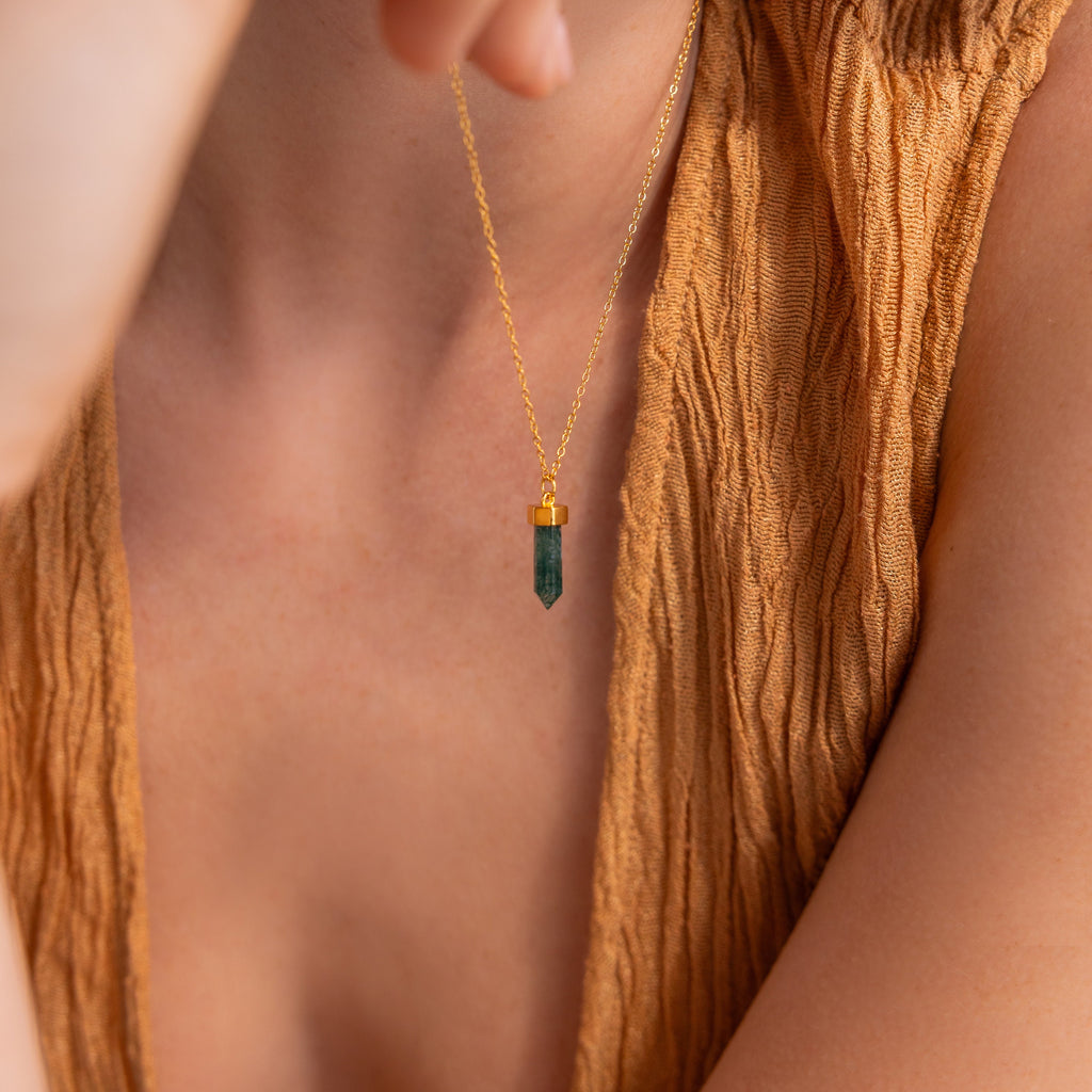 A woman in a textured tan top wears the Agate Quartz Necklace, featuring a gold chain and a green gemstone charm pendant.