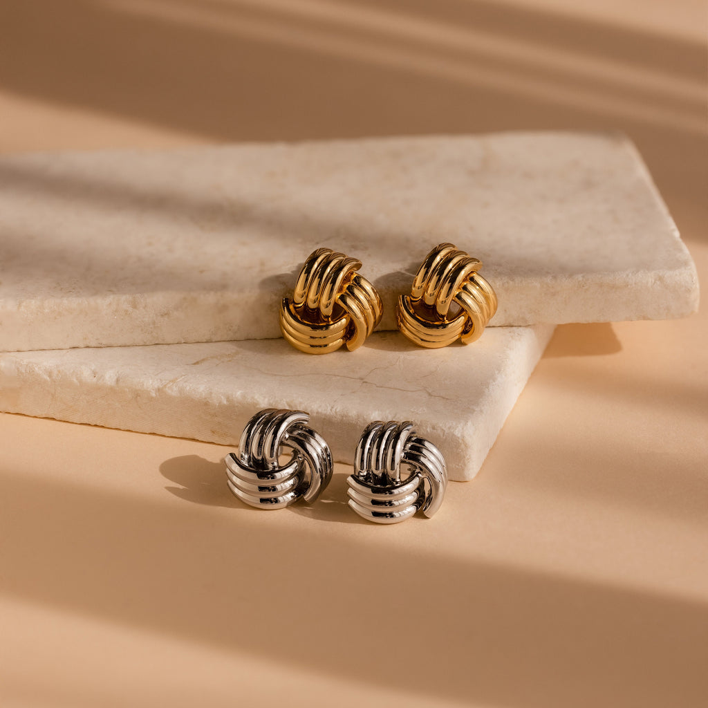Bold Triple Knot Studs, featuring a rope-inspired design in gold and silver, are displayed on two stacked marble slabs.