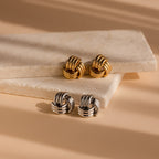 Bold Triple Knot Studs, featuring a rope-inspired design in gold and silver, are displayed on two stacked marble slabs.