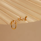 The Opal Cartilage Studs Set includes three small gold earrings with white and crystal accents, perfect for helix piercings, displayed on a beige fan-shaped surface.