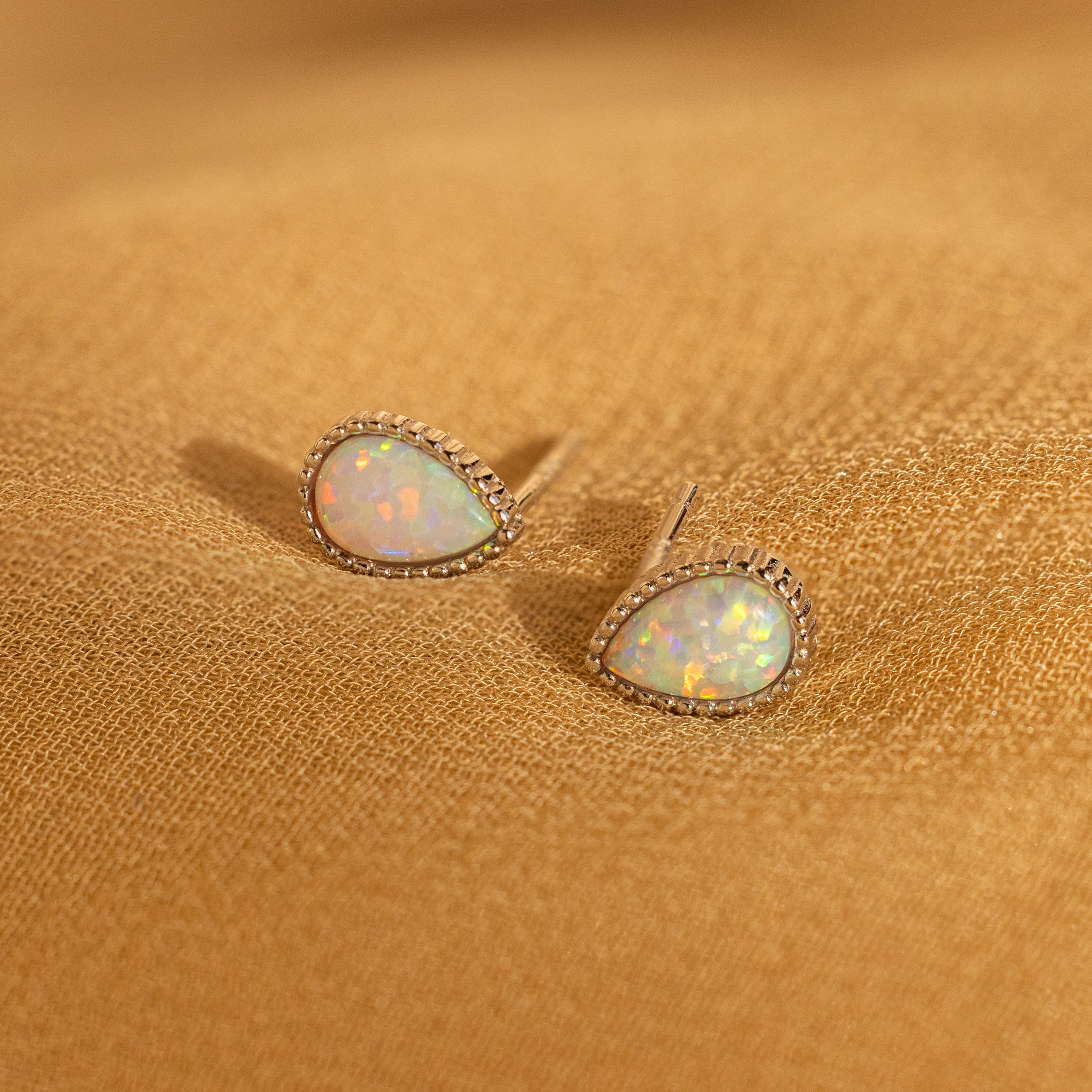 Opal Teardrop Studs, shown on textured golden fabric, are a stunning piece of vintage-inspired jewelry perfect for statement jewelry lovers.