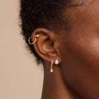 Close-up of a person's ear with three gold earrings, including a hoop and two dangle earrings—one pair is the Opal Teardrop Studs, bringing vintage-inspired elegance and gemstone sparkle for a standout jewelry look.