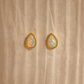 Opal Teardrop Studs shine on a textured beige backdrop—elegant, vintage-inspired jewelry with gold trim, perfect for making a statement.