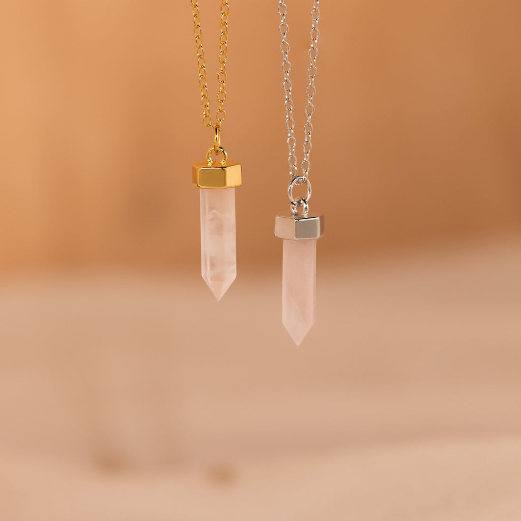 Two Rose Quartz Necklace pendants with gold and silver chains hang gracefully on a soft beige background, highlighting the elegant style of this stone of love.