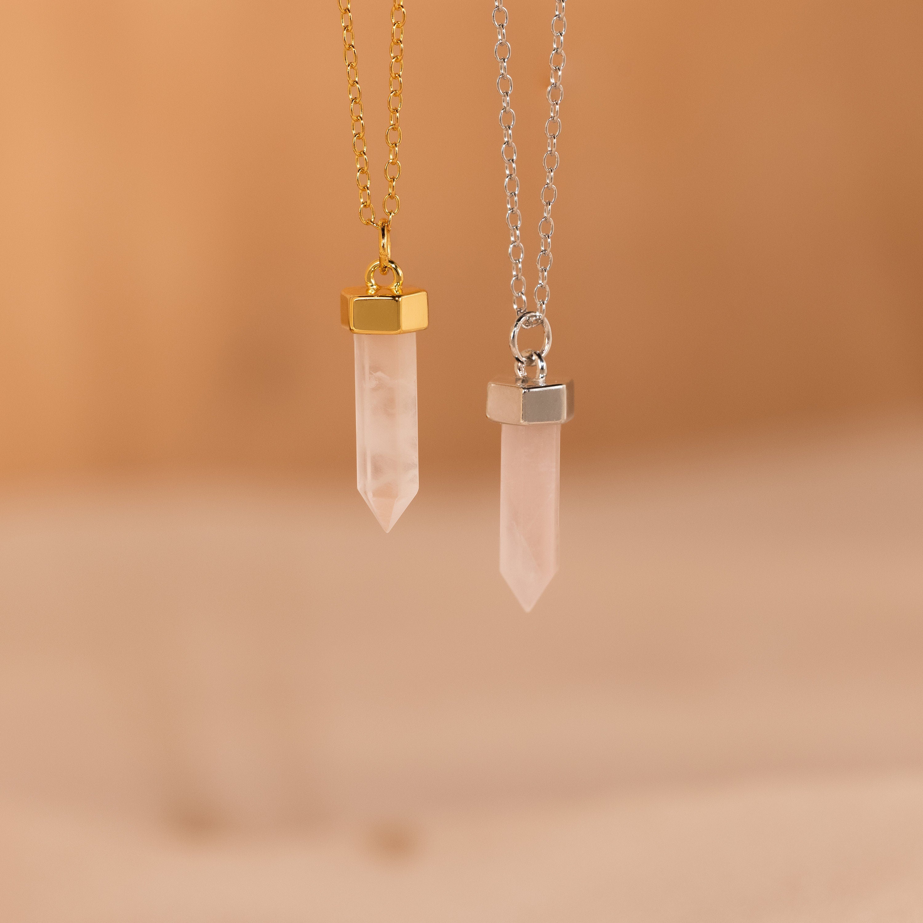 Two Rose Quartz Necklace pendants with gold and silver chains hang gracefully on a soft beige background, highlighting the elegant style of this stone of love.