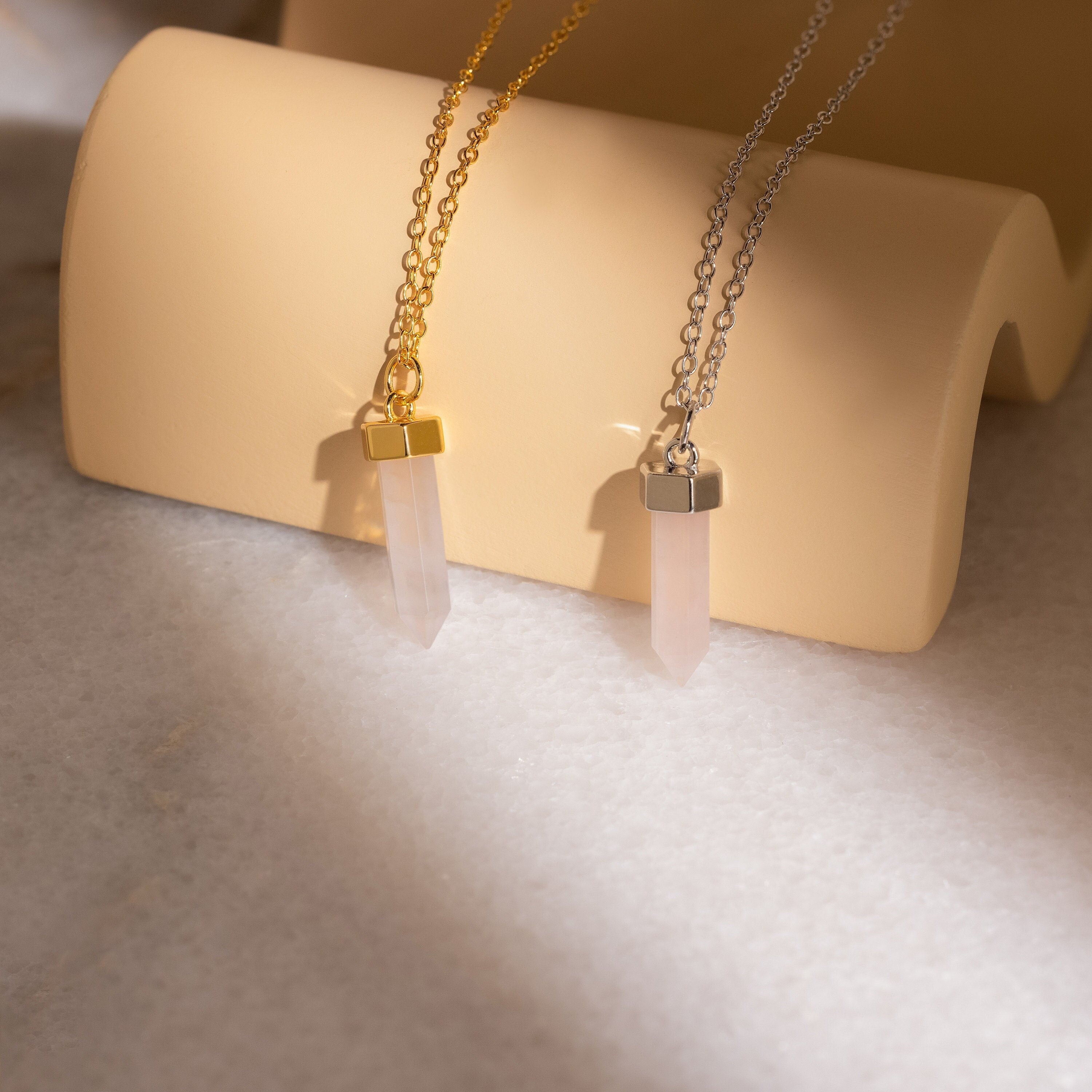 The Rose Quartz Necklace, known as the stone of love, is beautifully displayed on a beige stand with both gold and silver chain options.