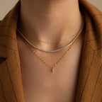 A person wearing three layered gold and silver necklaces, featuring the Dainty Marquise Pendant Necklace, paired with a brown pinstripe blazer.