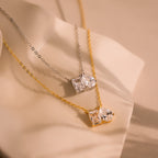 The Toi et Moi Diamond Necklace features two elegant pendants—one silver with an emerald-cut diamond, and one gold with a teardrop-shaped diamond—displayed on a soft background.