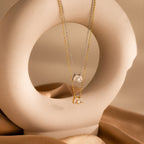 The Toi et Moi Diamond Necklace comes in both gold and silver, featuring a sparkling teardrop-shaped diamond, elegantly displayed on a smooth, circular beige sculpture.