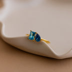 Toi et Moi Birthstone Ring in Rose Gold featuring two blue gemstones—one square, one teardrop—set on a wavy dish. Customizable and perfect as a unique Christmas gift.