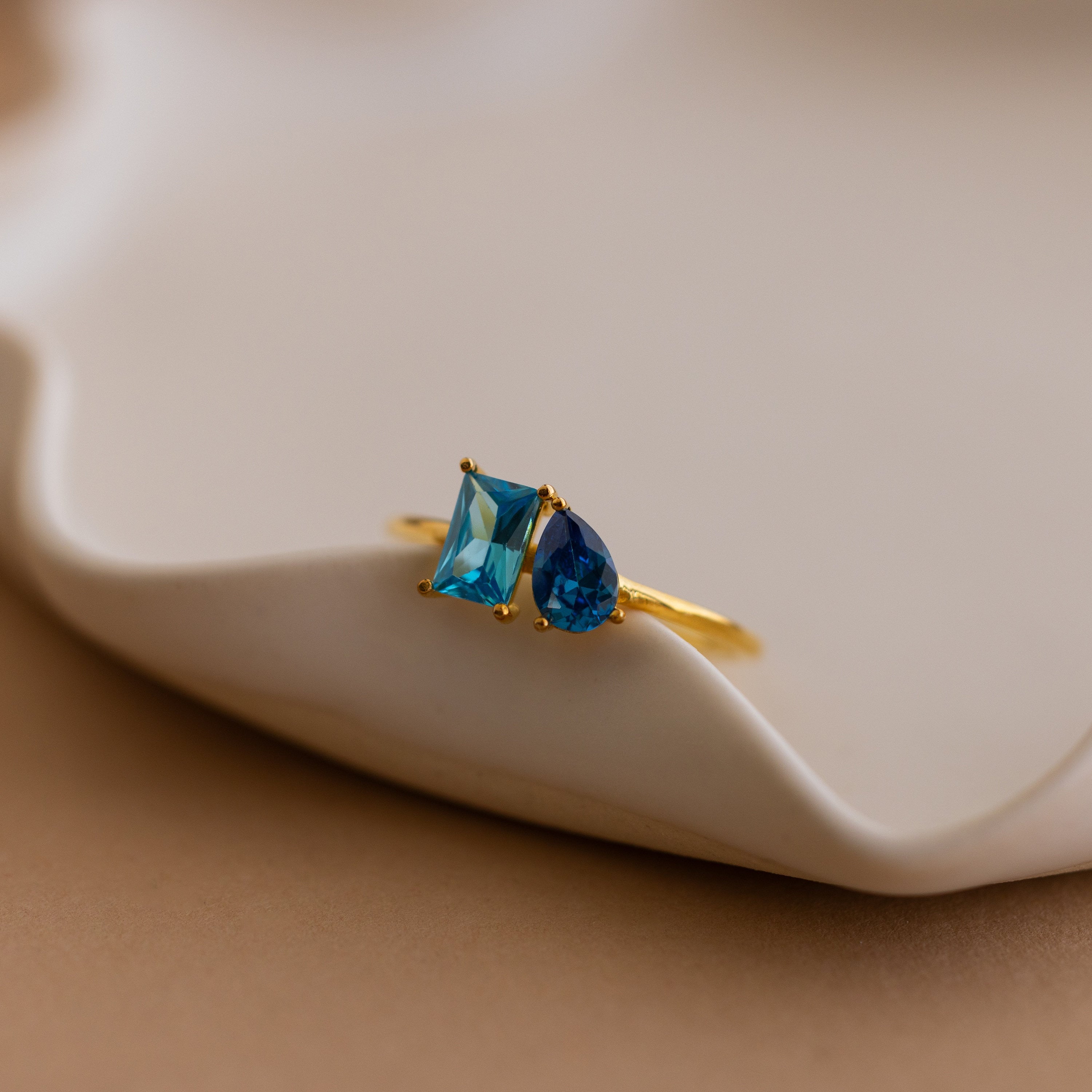 Toi et Moi Birthstone Ring in Rose Gold featuring two blue gemstones—one square, one teardrop—set on a wavy dish. Customizable and perfect as a unique Christmas gift.