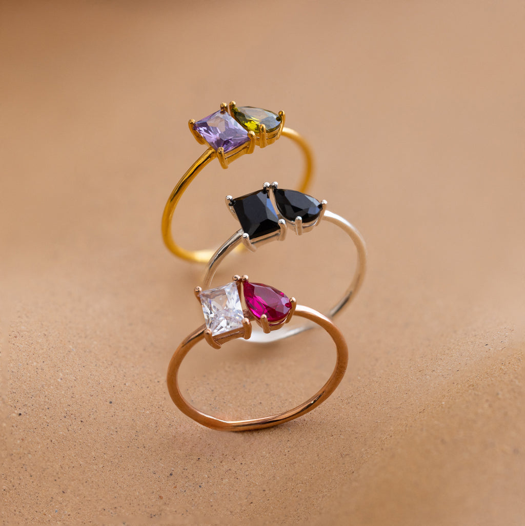 The Toi et Moi Birthstone Ring in Rose Gold features customizable gemstones set on a sleek band—an ideal, personalized Christmas gift displayed elegantly on a smooth beige surface.