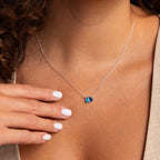 Someone wearing the Toi et Moi Birthstone Necklace, featuring a blue fish pendant, with their hand resting near the chain.