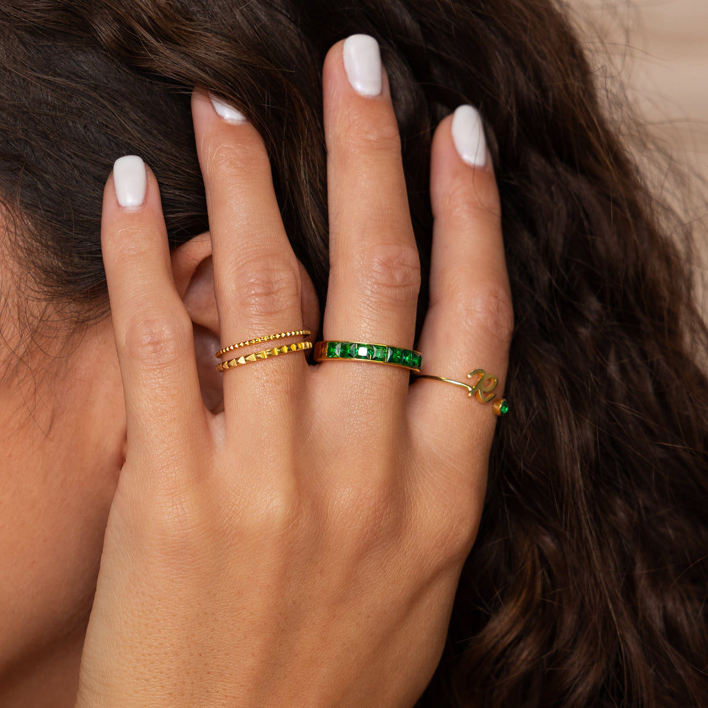 A hand with white nail polish wears three gold rings, including the striking Birthstone Inlay Band, near curly brown hair—a true statement accessory.