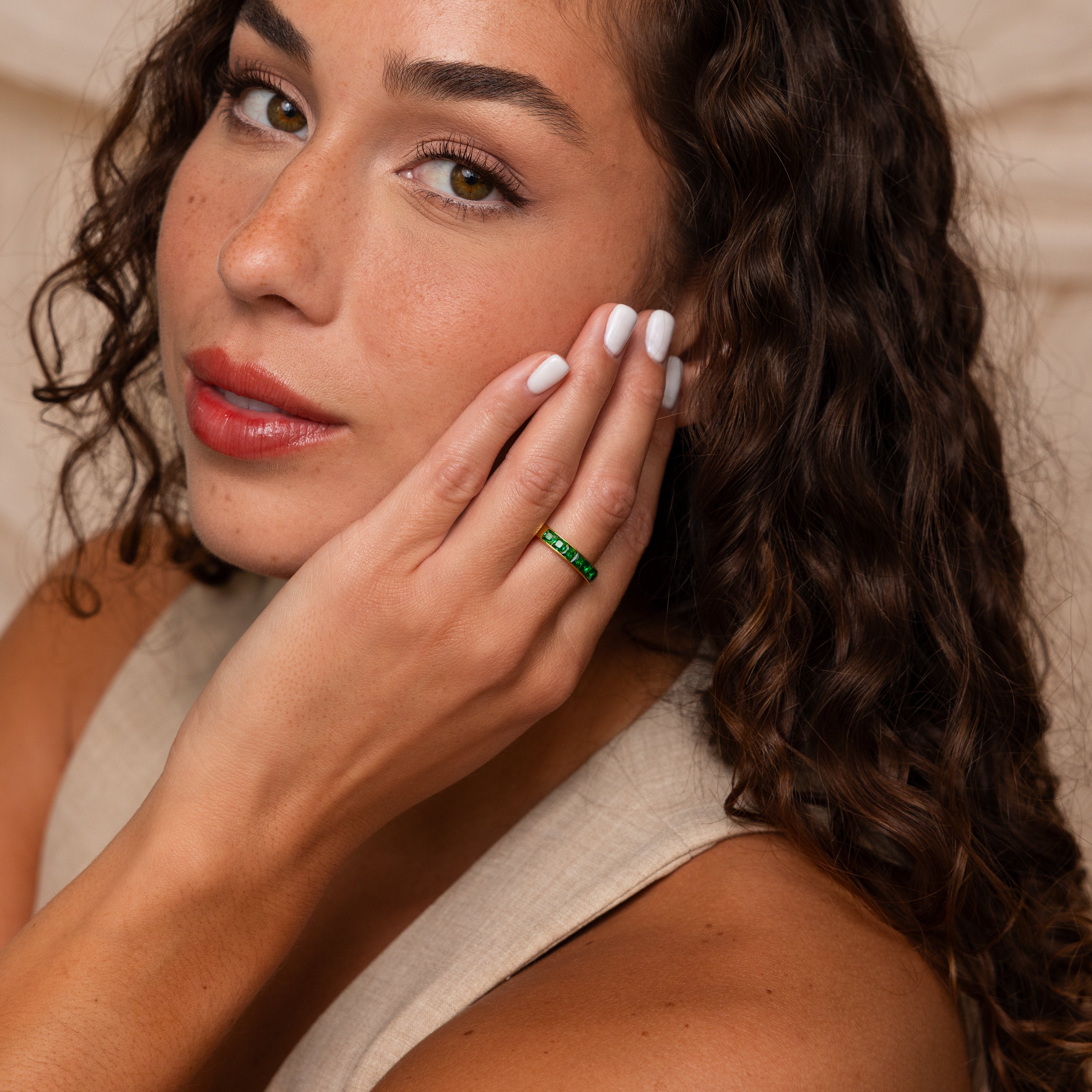 A woman with curly hair touches her face, showcasing the green Birthstone Inlay Band—a bold accessory—paired with a neutral sleeveless top.