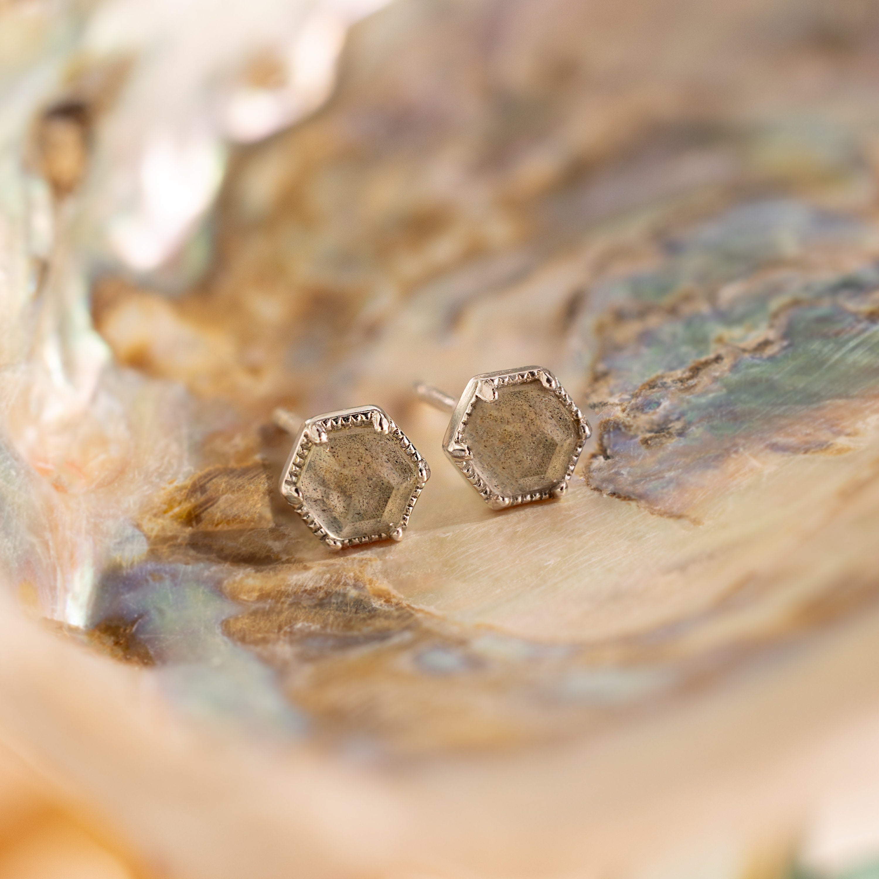 Labradorite Hexagon Studs with a metallic finish sit atop an iridescent, textured surface, bringing a mystical touch to your jewelry collection.