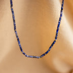 Close-up of the Tanzanite Beaded Necklace, showcasing tanzanite blue beads with gold accents on a soft beige fabric background.