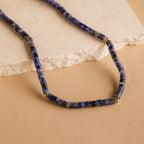 The Tanzanite Beaded Necklace, accented with gold spacers and vibrant blue beads, is beautifully showcased on a beige stone and tan background—ideal for fans of mystical jewelry.
