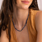 A woman in a textured mustard top smiles softly, wearing the Tanzanite Beaded Necklace—its tanzanite blue beads adding a touch of mystical charm.