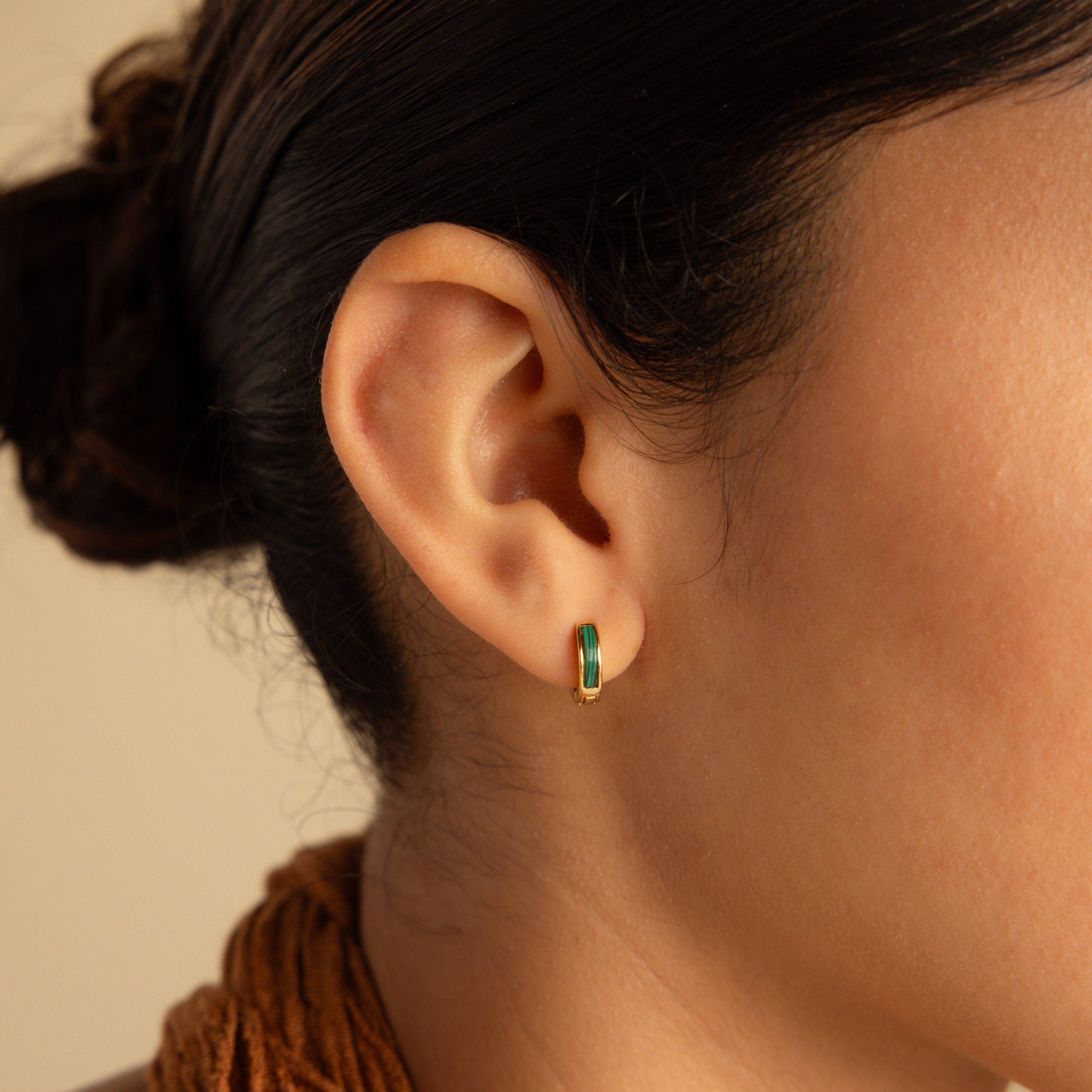 Close-up of a woman's ear adorned with Malachite Inlay Huggies—small gold hoop earrings featuring green malachite, ideal for lovers of green stone jewelry.