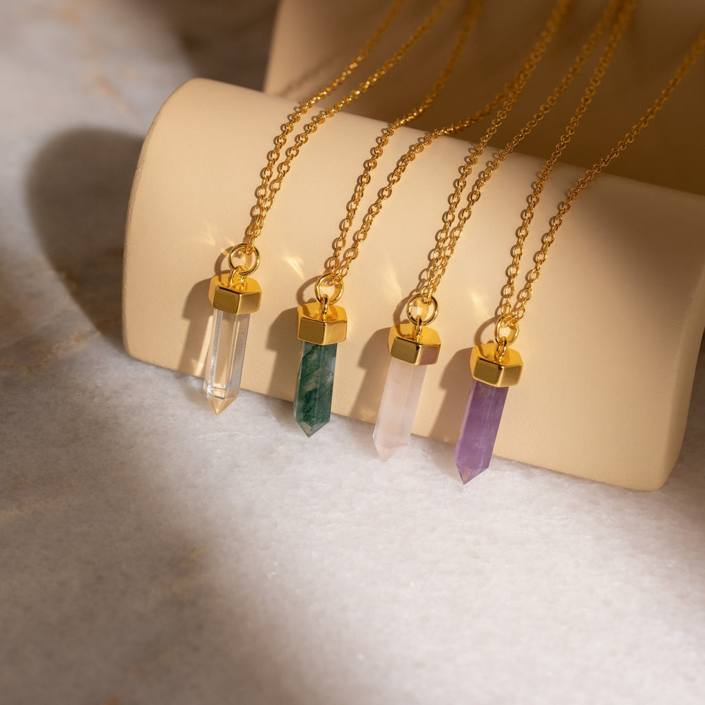 Crystal Quartz Necklaces: Four gold chain necklaces with hexagonal point pendants in clear, green, pink, and purple quartz are displayed on a roll—ideal for adding positive energy to your style.