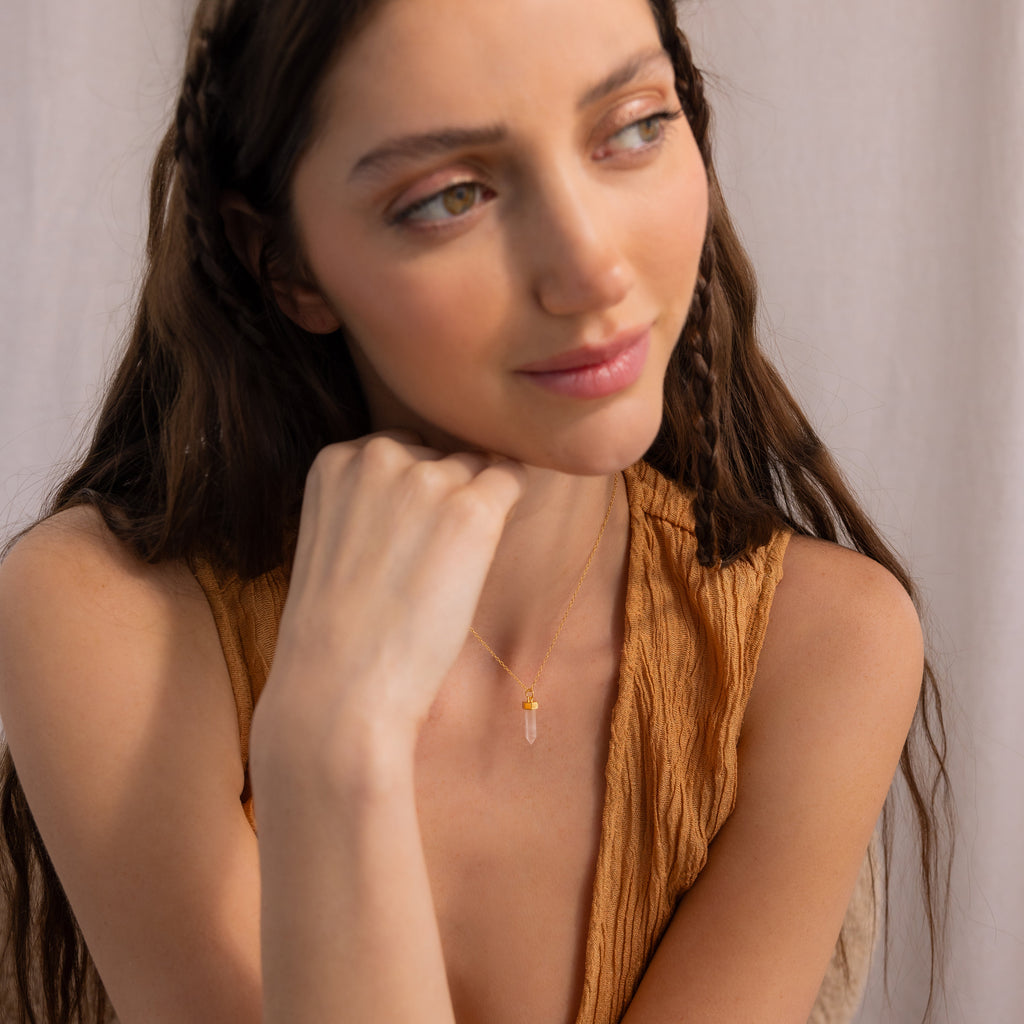 A woman with long brown hair wearing a sleeveless tan top and the Rose Quartz Necklace, known as the stone of love, gazes to the side.