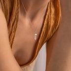 A person wearing the Rose Quartz Necklace, a silver chain featuring the stone of love with a clear crystal pendant, paired with a brown textured top.