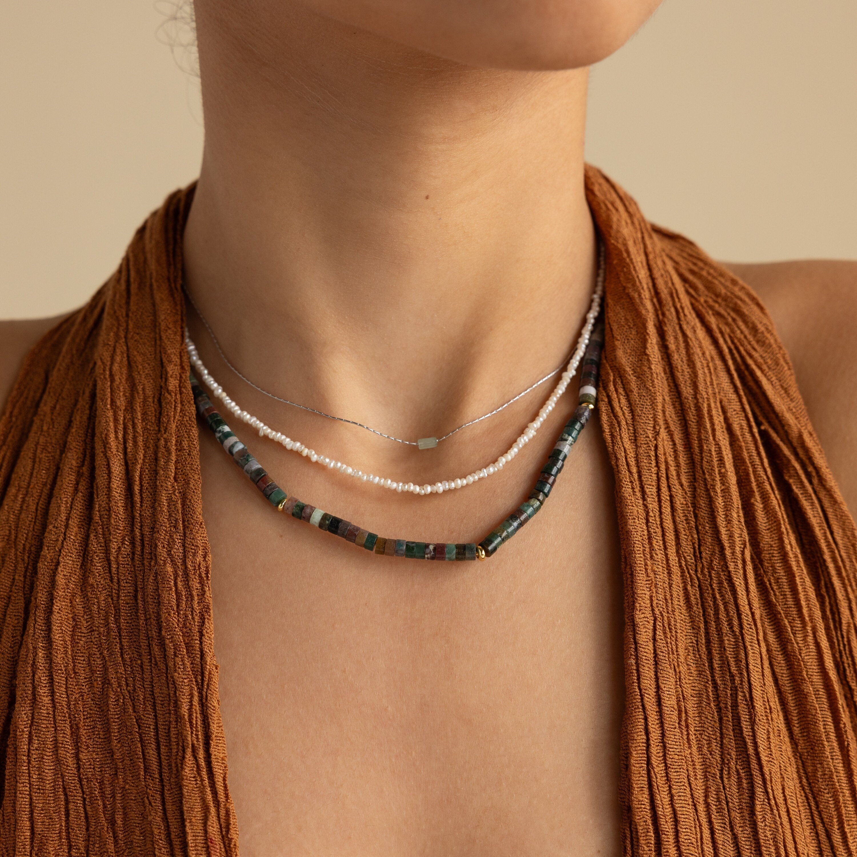 A woman radiates earthy elegance wearing a brown textured sleeveless top and three layered necklaces, including the Moss Agate Beaded Necklace.