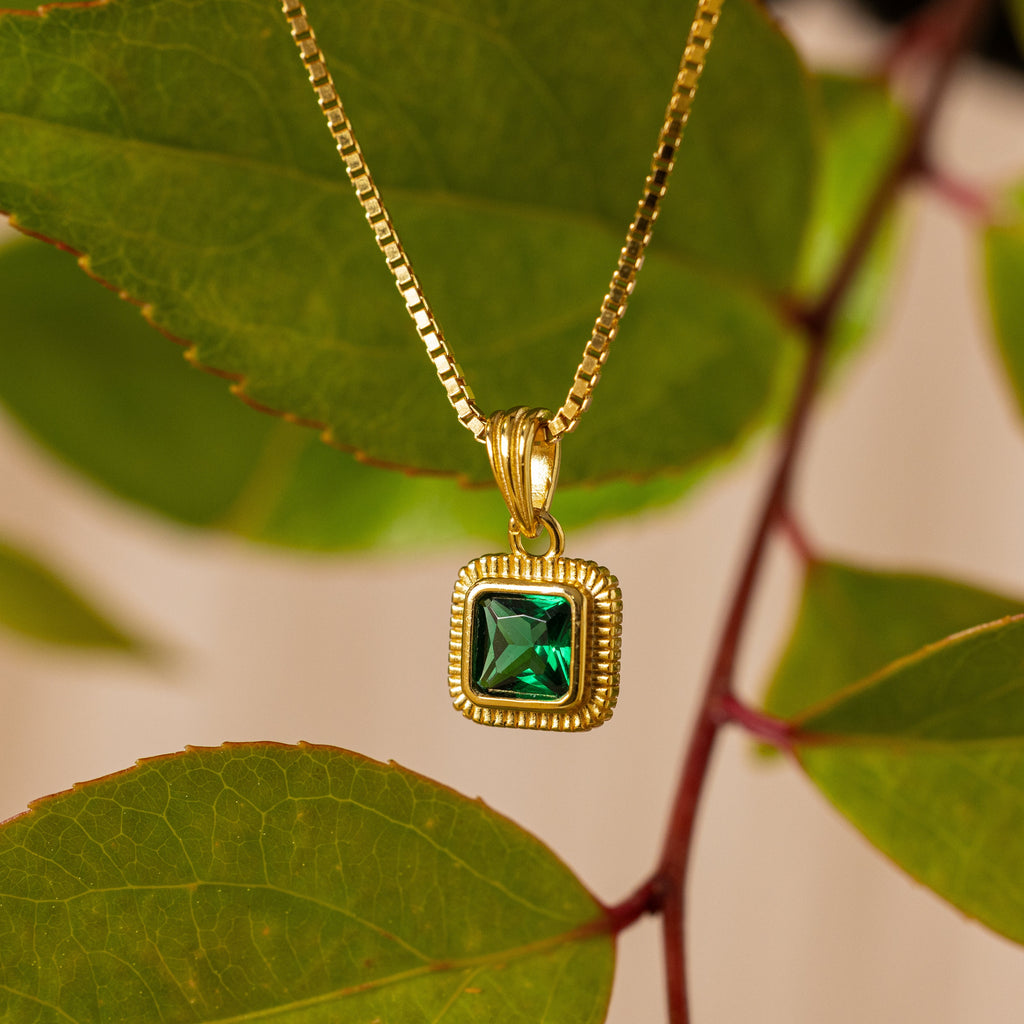 The Vintage Emerald Pendant Necklace features a square emerald gemstone on a gold chain, displayed with green leaves for a vintage Art Deco look—an elegant choice for timeless style.