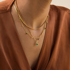 A person wearing layered gold necklaces, including a Vintage Emerald Pendant Necklace, and a brown V-neck blouse.