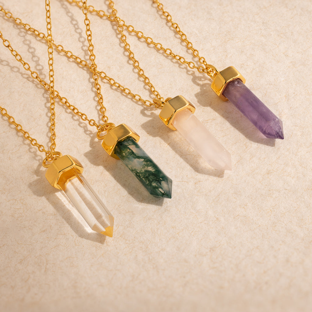 Four Amethyst Quartz Necklaces with gold chains and settings, each featuring a stunning crystal charm, displayed on a light beige textured surface—a unique gift for any occasion.