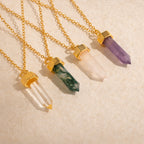 Four Amethyst Quartz Necklaces with gold chains and settings, each featuring a stunning crystal charm, displayed on a light beige textured surface—a unique gift for any occasion.