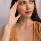 Woman holding her hand to her face, wearing the Amethyst Quartz Necklace featuring a purple crystal charm pendant and a textured tan top—a truly unique gift idea.