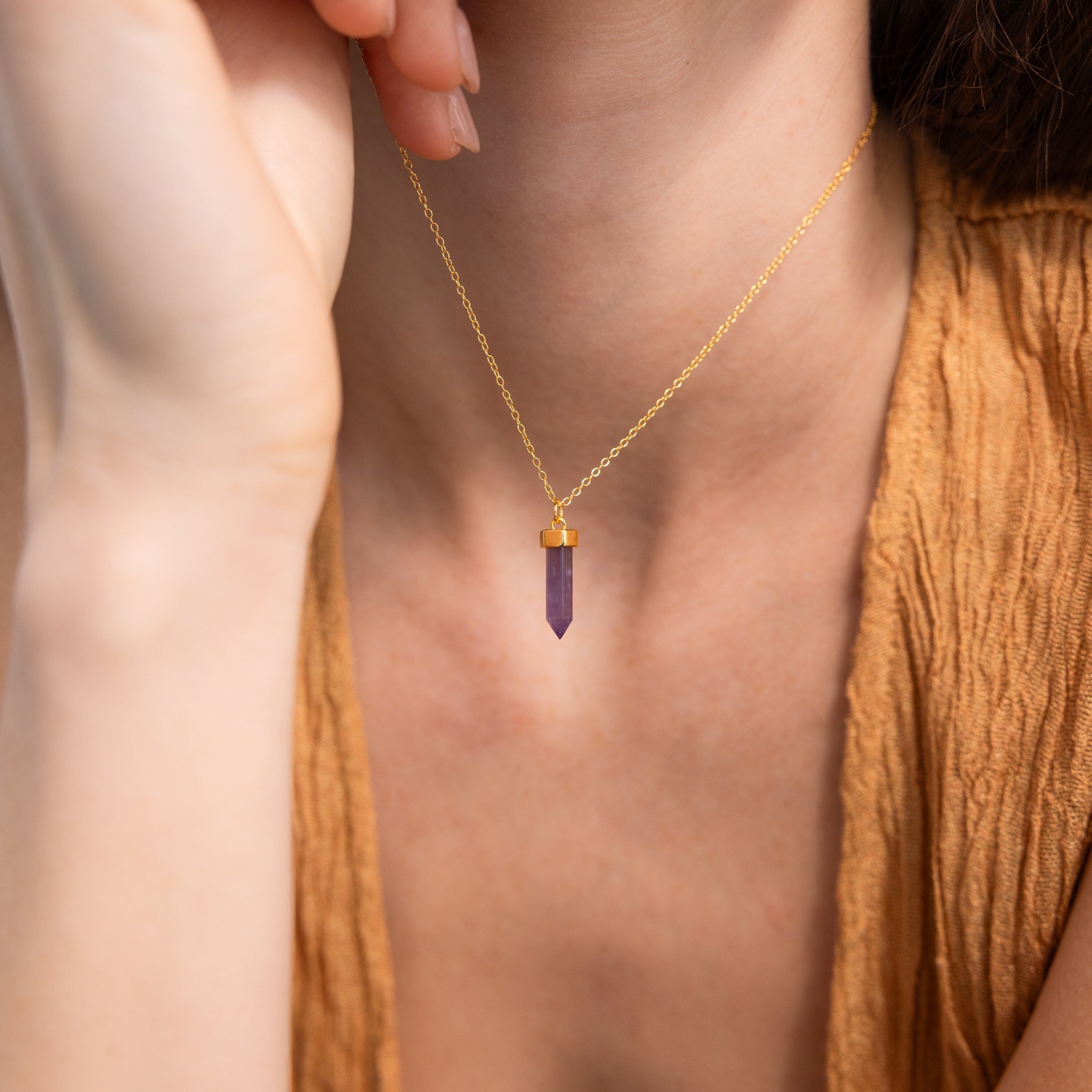 A woman wears the Amethyst Quartz Necklace with a purple crystal pendant, paired with a textured brown top.