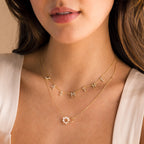 A woman wears two gold necklaces—one spelling JASMINE and one with a small flower charm—paired perfectly with the Interlocking Pearl Necklace against bare skin.
