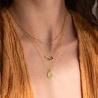Woman wearing the Pave Fingerprint Coin Necklace, a three-layered gold piece with a custom engraved pendant, styled over a textured tan V-neck top.