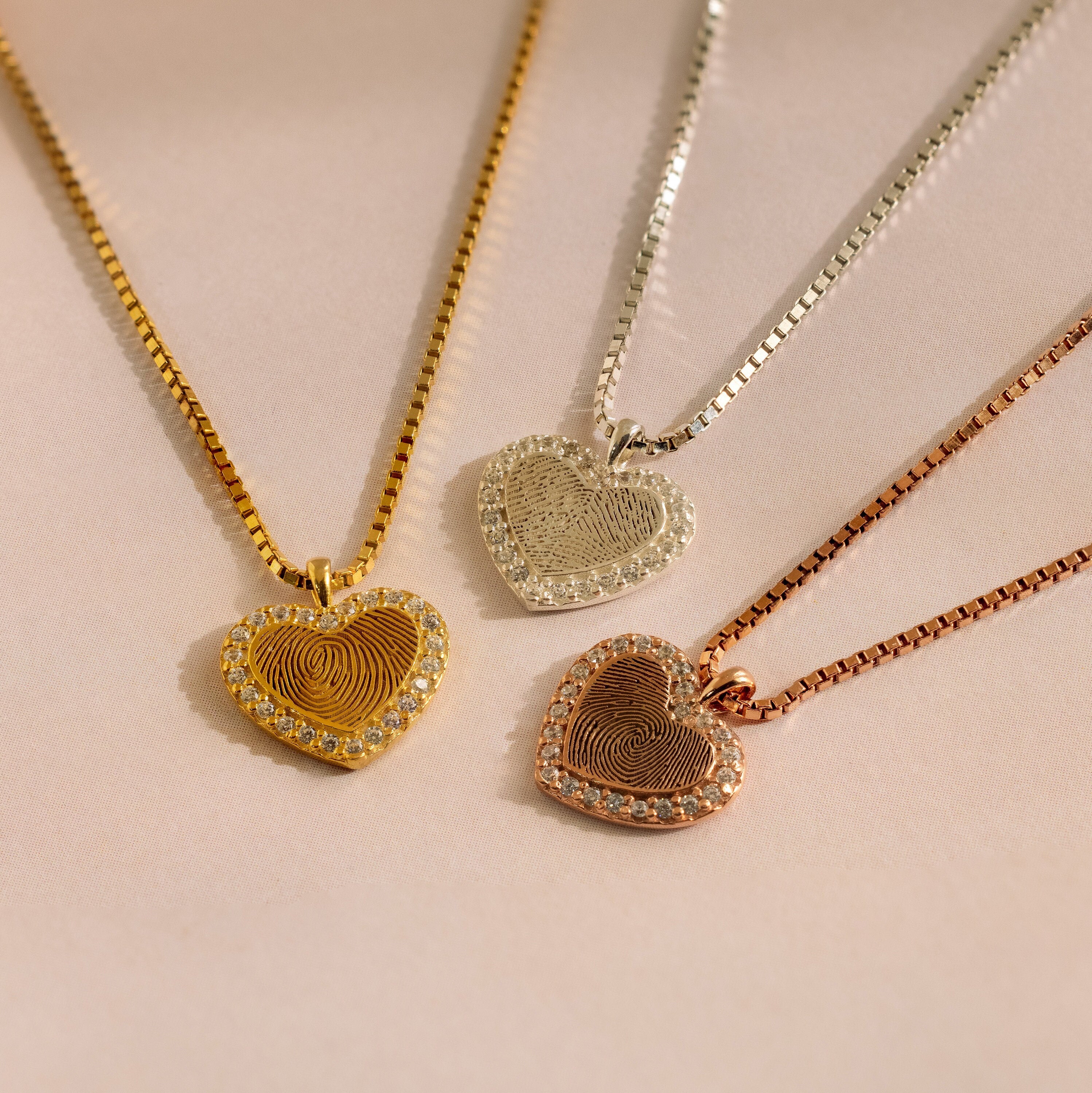 The Pave Fingerprint Heart Necklace comes in gold, silver, and rose gold with a personalized engraved fingerprint heart pendant and sparkling gem accents.