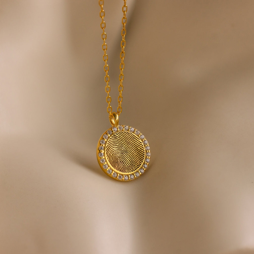 The Pave Fingerprint Coin Necklace features a round pendant engraved with a custom fingerprint and bordered by sparkling stones—an elegant, personalized memorial gift.