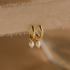 Close-up of Dainty Gold Pearl Huggies hanging from a sheer beige fabric.
