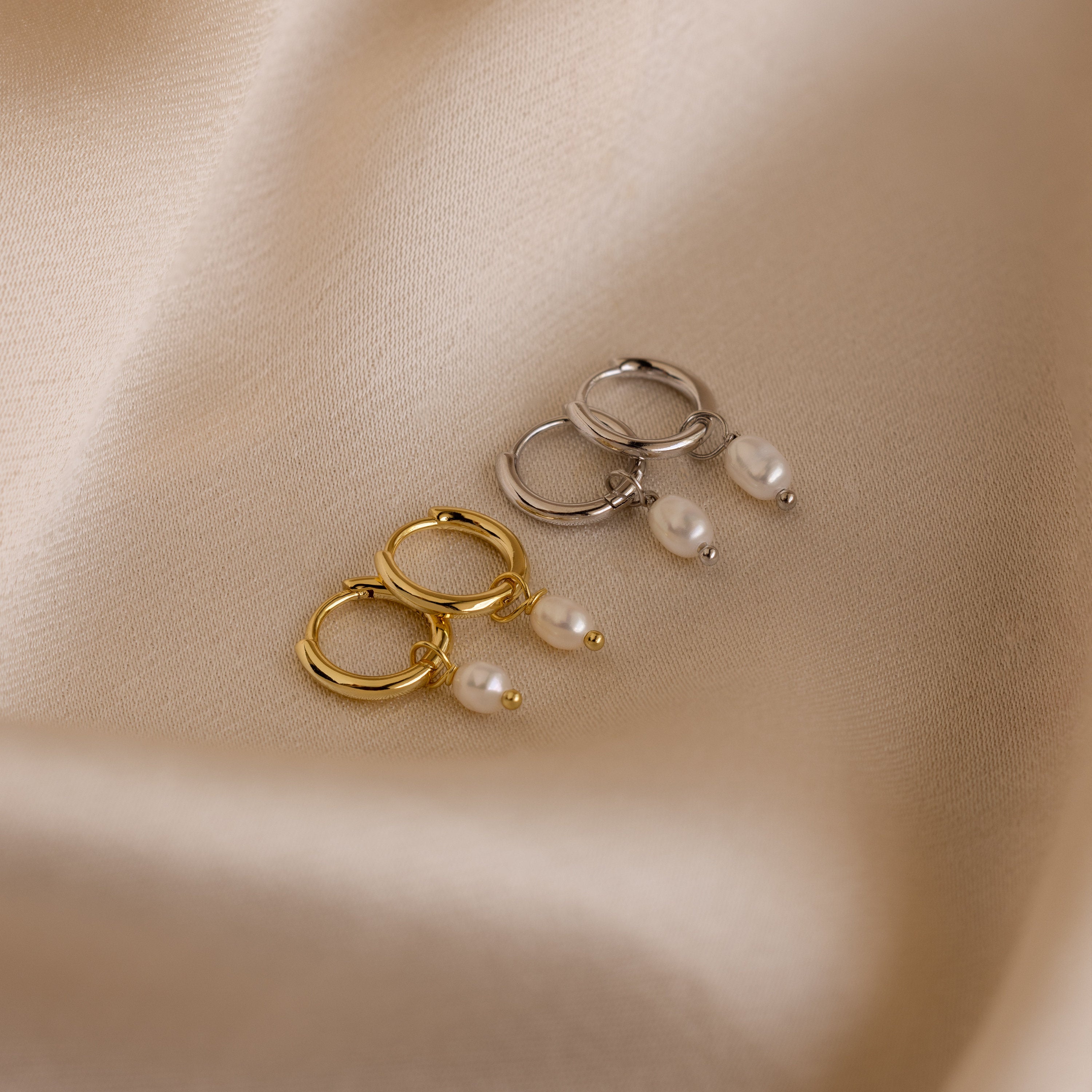Close-up of Gold and Silver Pearl Huggie earrings on a satin fabric.