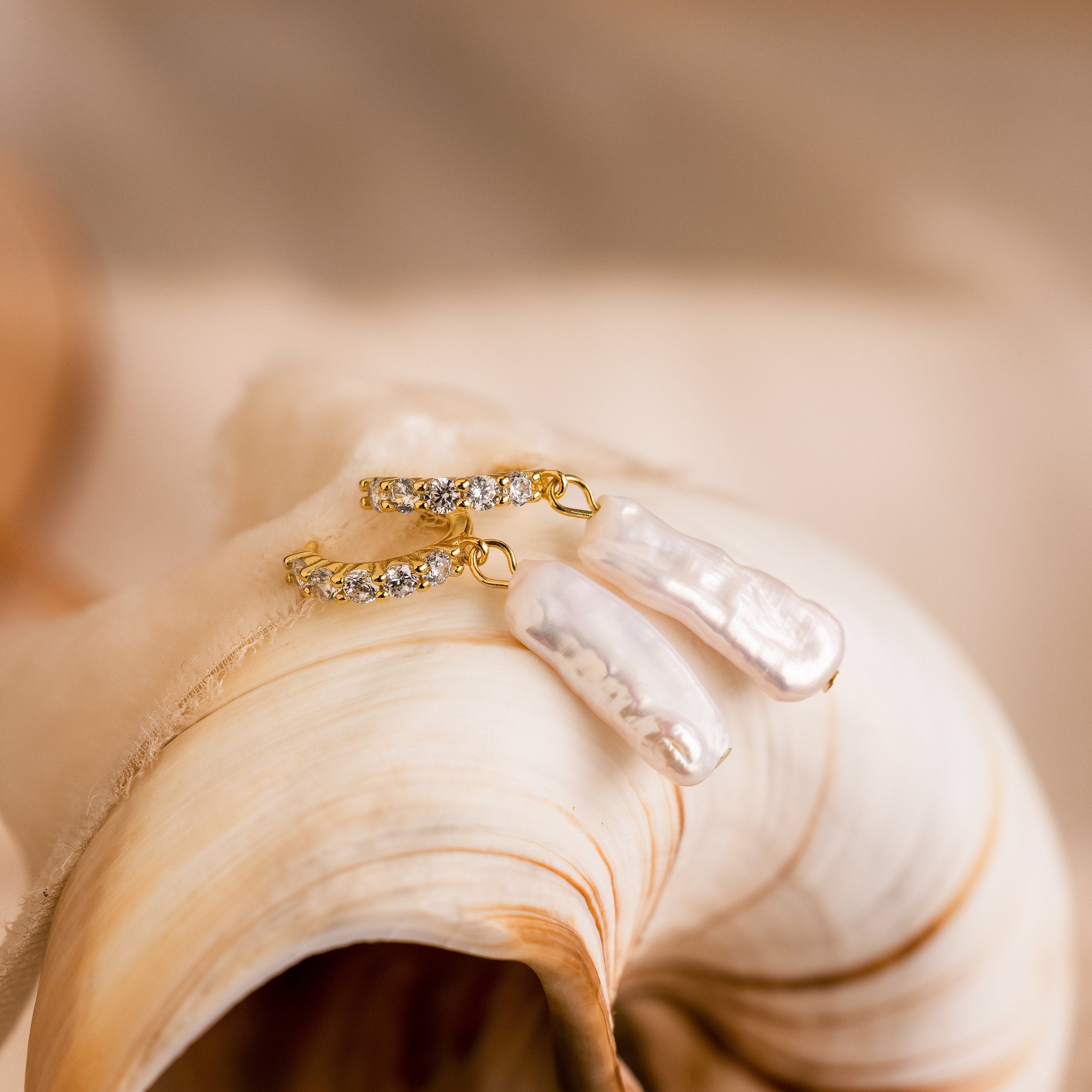 Baroque Pearl Pave Huggies, adorned with sparkling crystals, are elegantly displayed on a large ivory seashell.