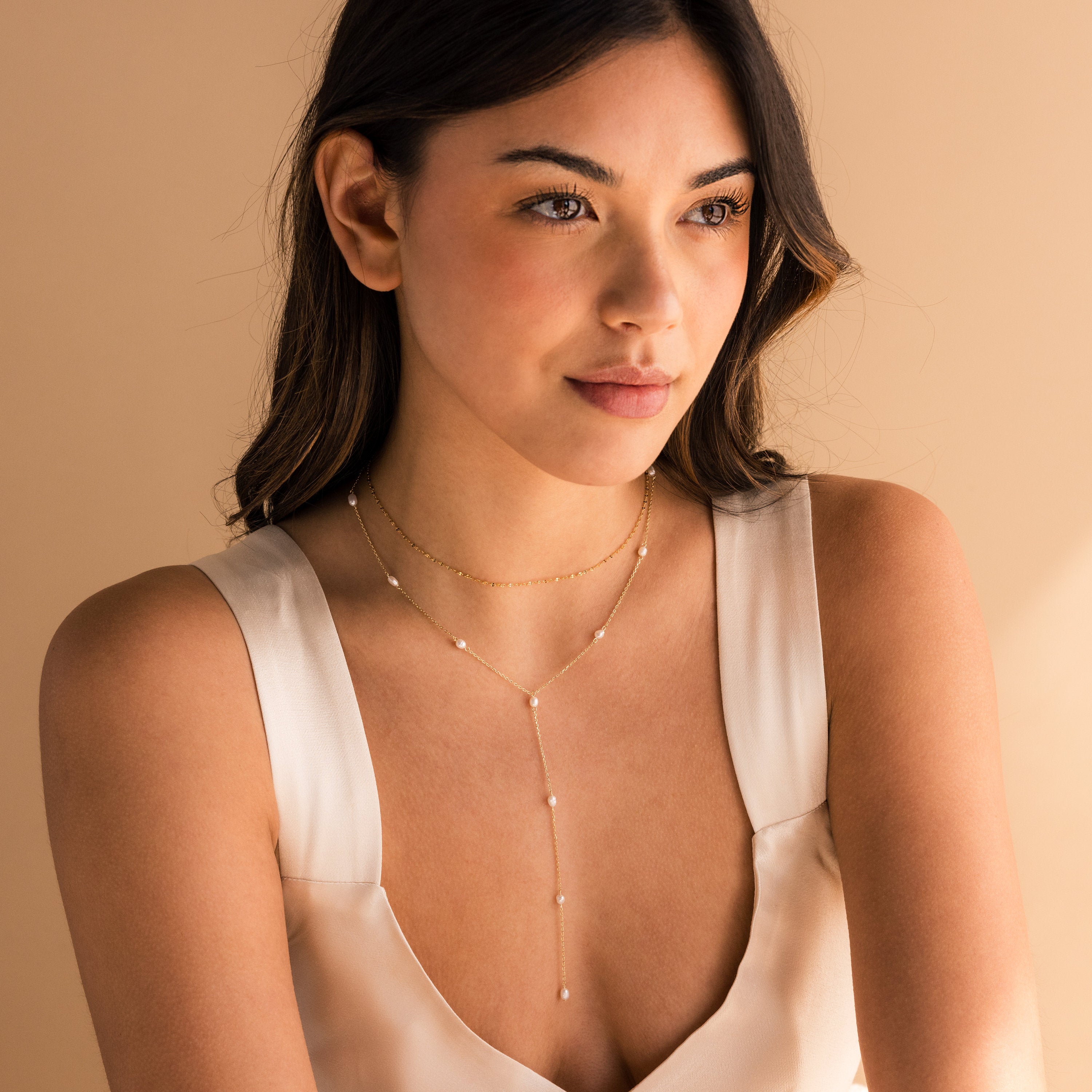 Woman wears a cream sleeveless top and the Pearl Station Lariat Necklace, a delicate gold lariat adorned with pearl charms.